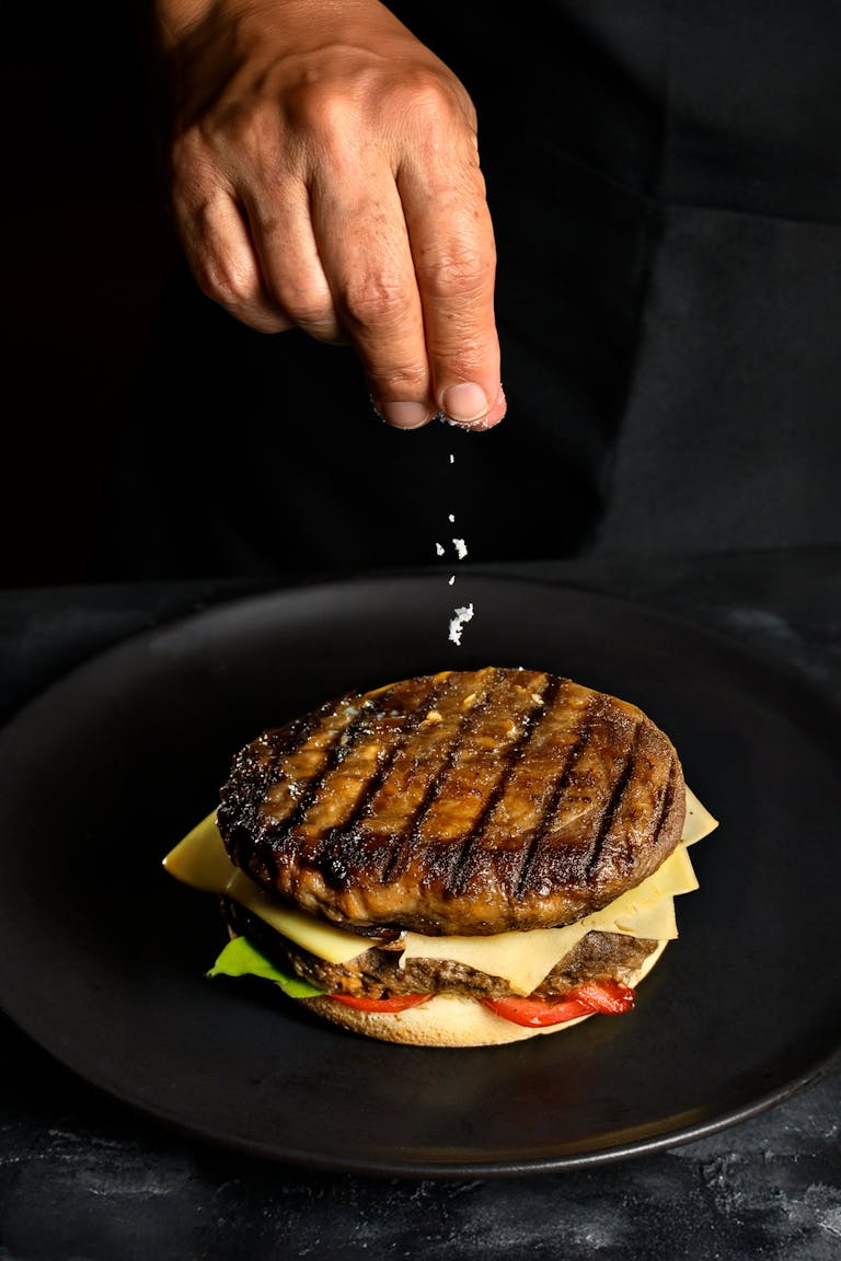 Close-up of a gourmet burger in Perú with a chef adding salt by hand, highlighting culinary artistry.