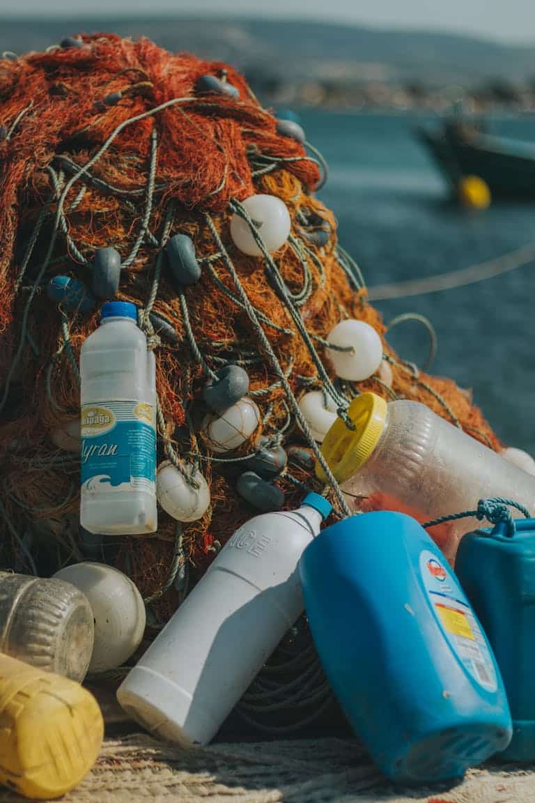 Close-up of fishing nets entangled with plastic bottles near the sea, illustrating marine pollution.