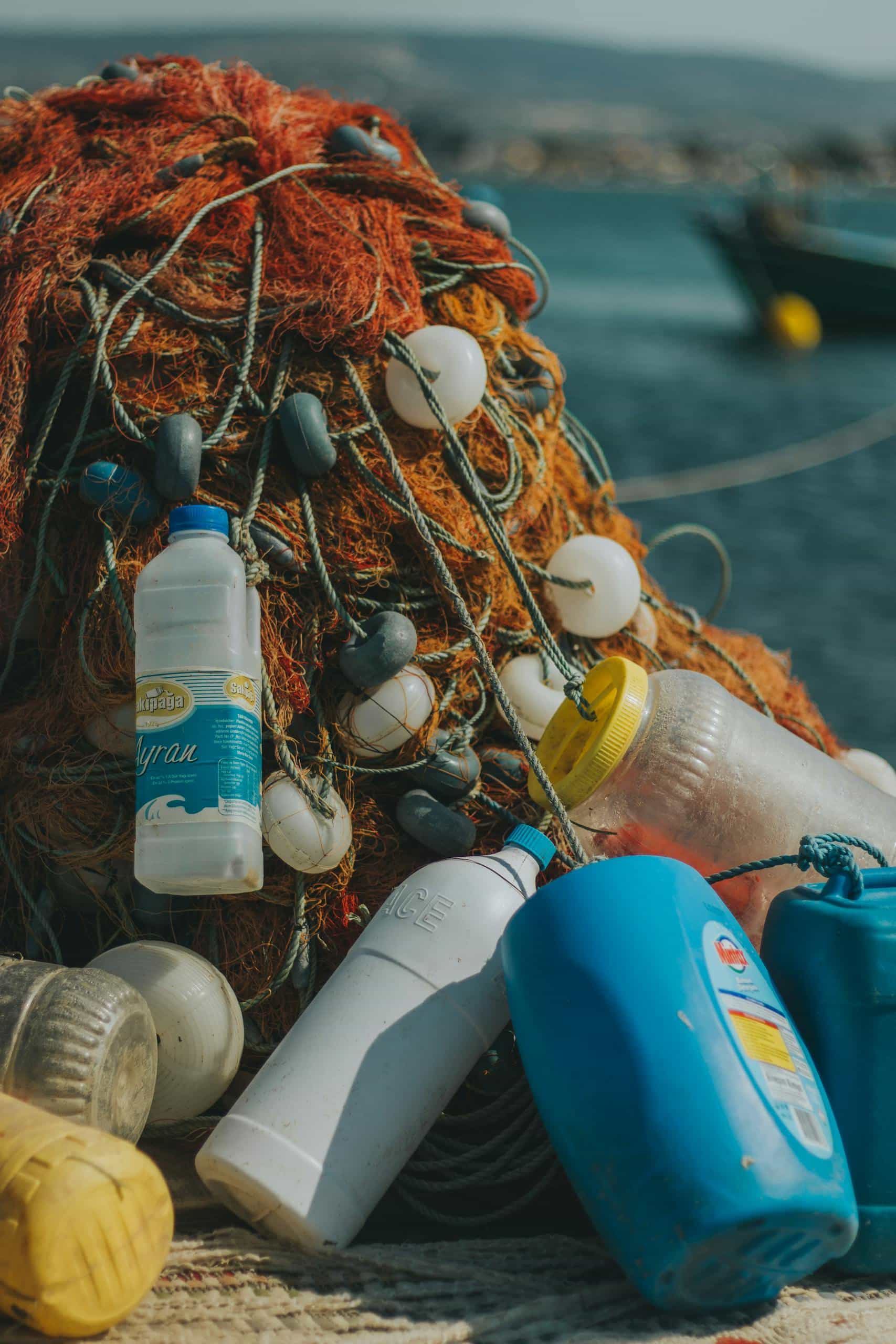 Close-up of fishing nets entangled with plastic bottles near the sea, illustrating marine pollution.
