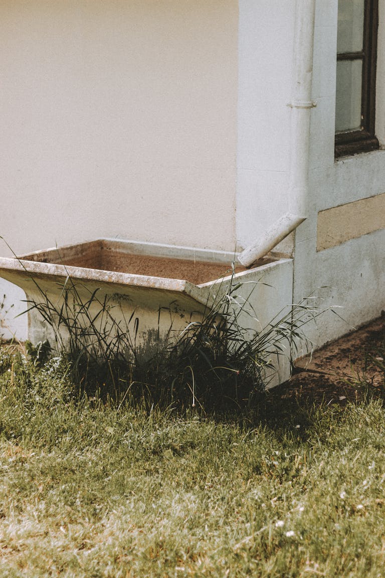 Exterior of shabby building with water tank placed under white pipe on grassy ground in summer