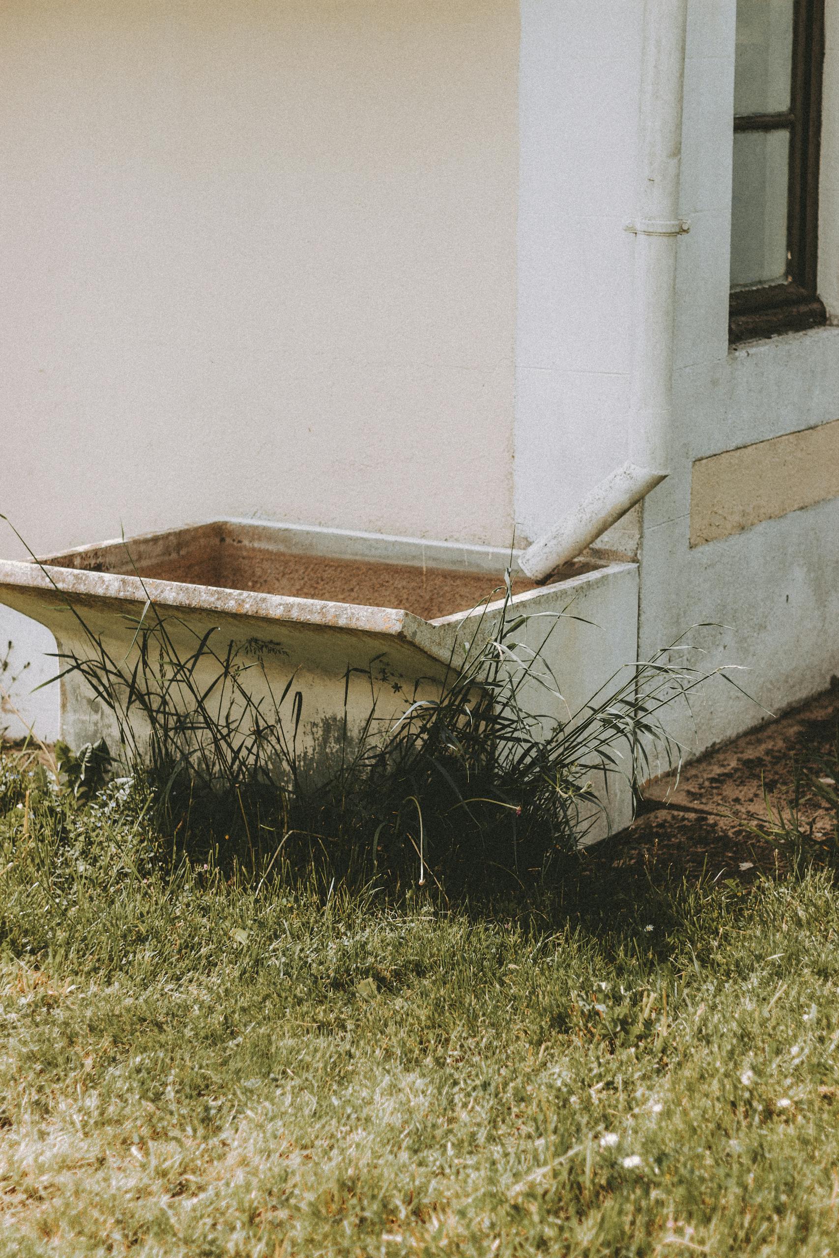 Exterior of shabby building with water tank placed under white pipe on grassy ground in summer