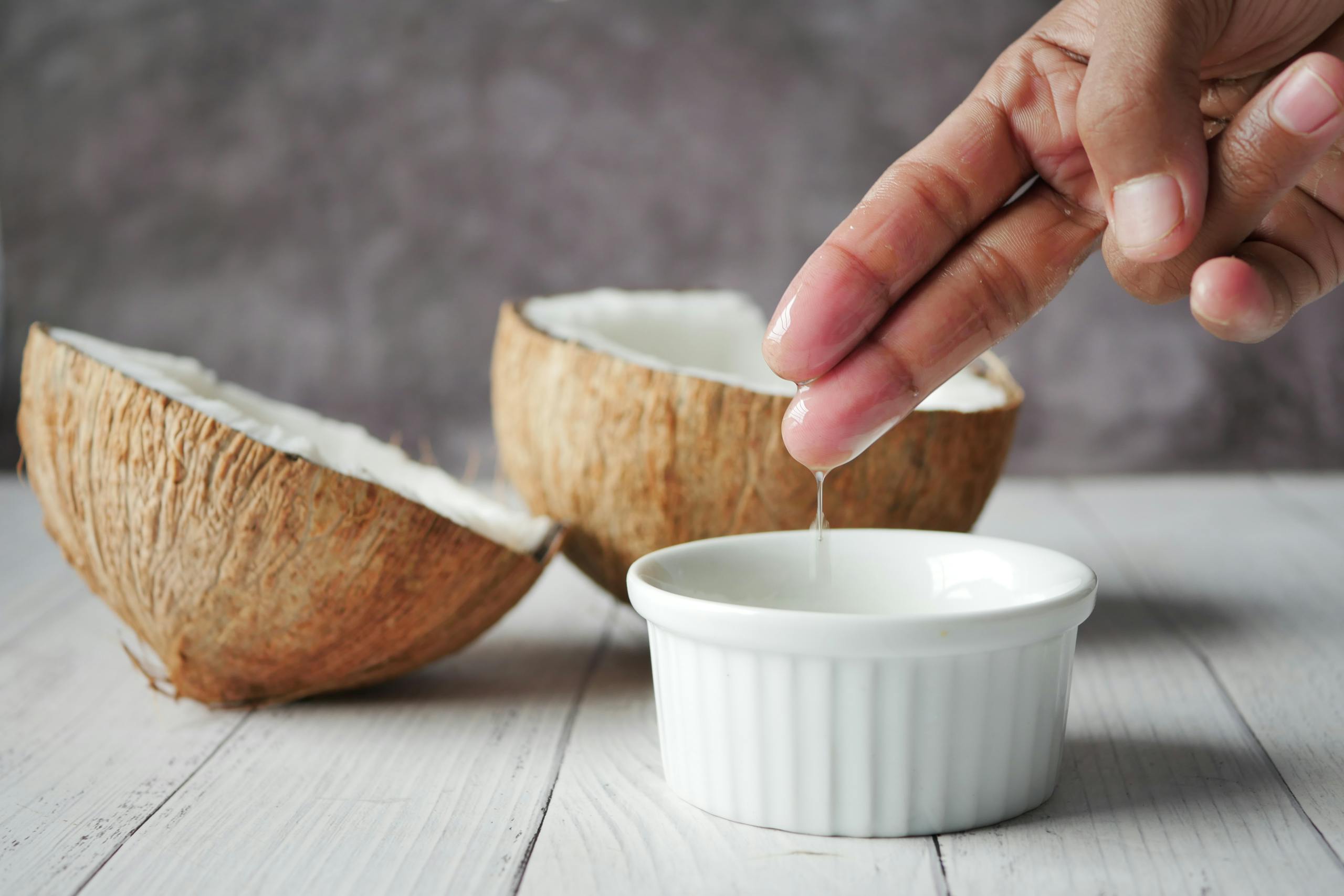 Hand extracting coconut oil into a bowl, ideal for natural skincare routines.
