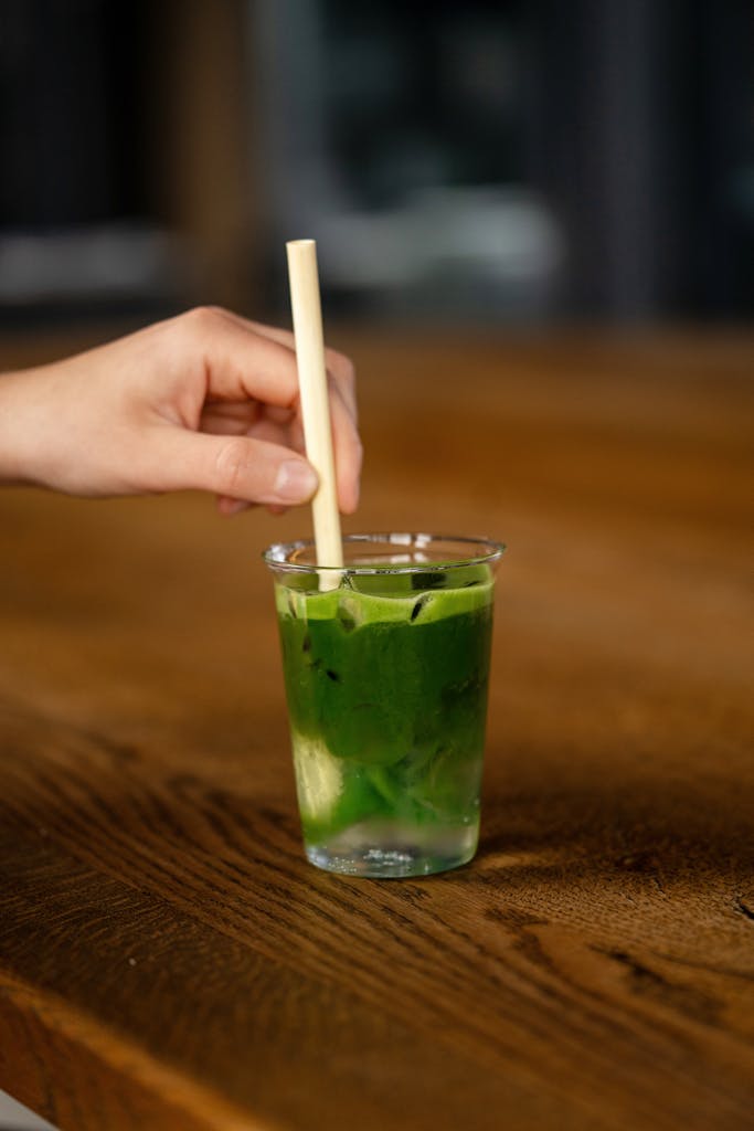 Close-up of a hand stirring an iced matcha drink with a straw. Refreshing and vibrant.