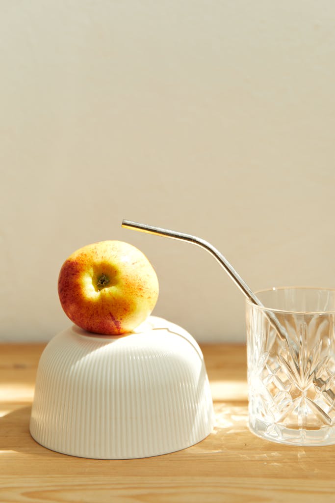 Elegant still life with an apple on a bowl and a crystal glass in sunlight.