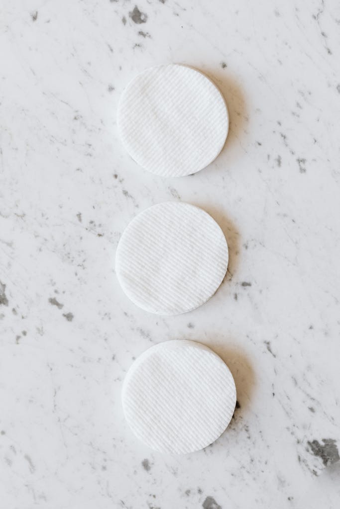 From above of row of clean round white cotton pads with smooth surface and soft texture on marble table with small spots and grey lines