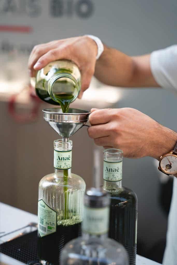 Man pouring green liquid through funnel into bottles at a Paris bar, creating a cocktail.