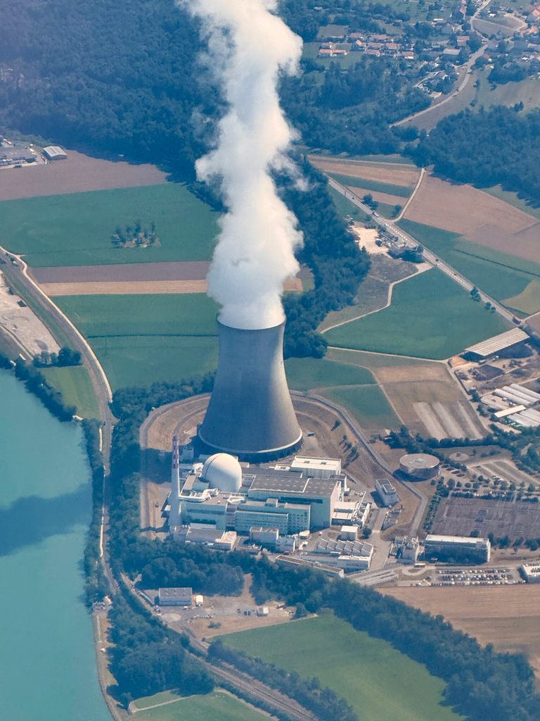 Aerial shot of a nuclear power plant with cooling tower emitting steam in Switzerland, captured in summer.